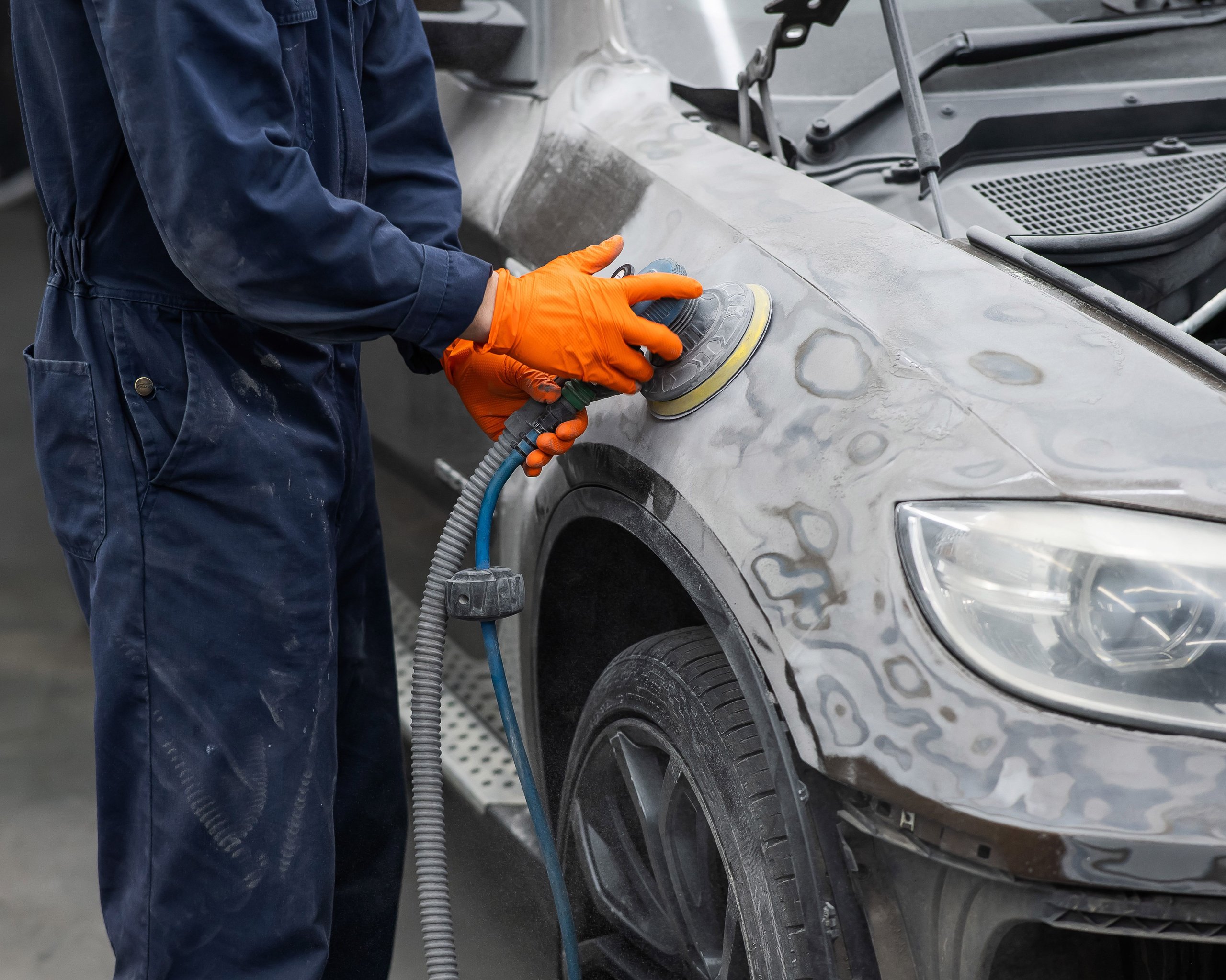 Mechanic machine-sanding a car panel during a precision repair