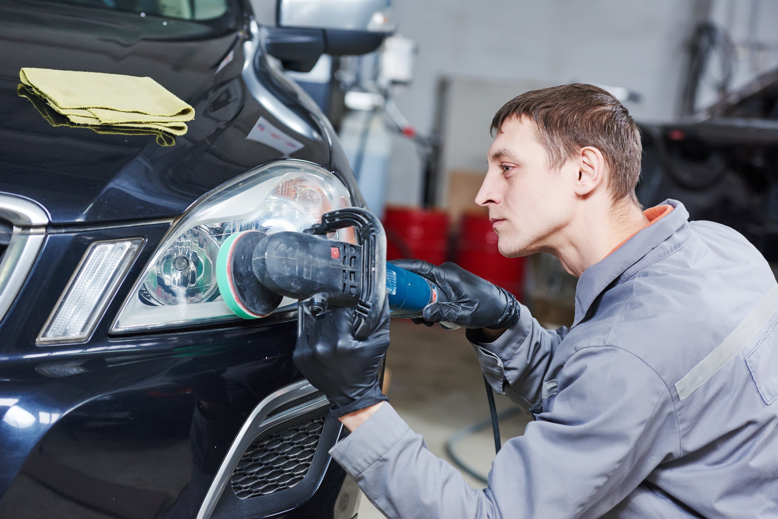 Mechanic buffing and polishing a car headlight in a garage workshop